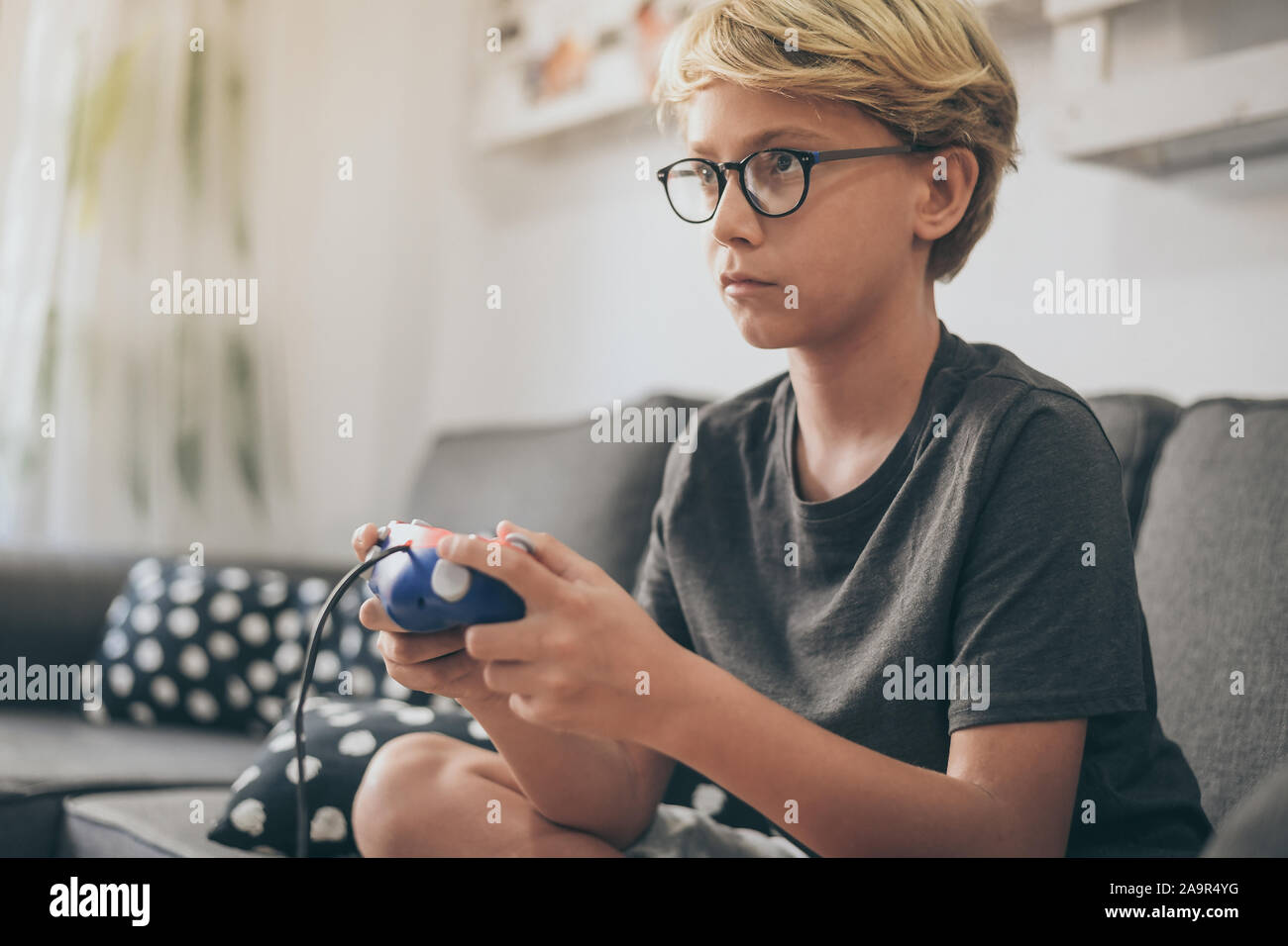 Garçon assis sur le canapé, jouant avec la console de jeu en ligne avec des amis. Teen sur le canapé fait grimace alors qu'il participait à un jeu vidéo. Addicted gamer en Banque D'Images