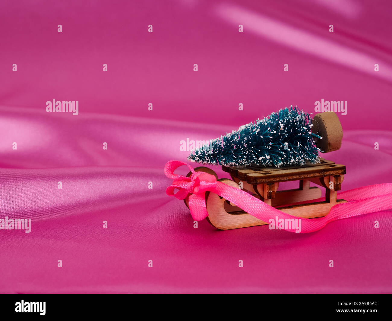 Arbre de Noël sur un traîneau sur un fond de satin rose brillant comme fond, fond de soie, carte de Noël Banque D'Images