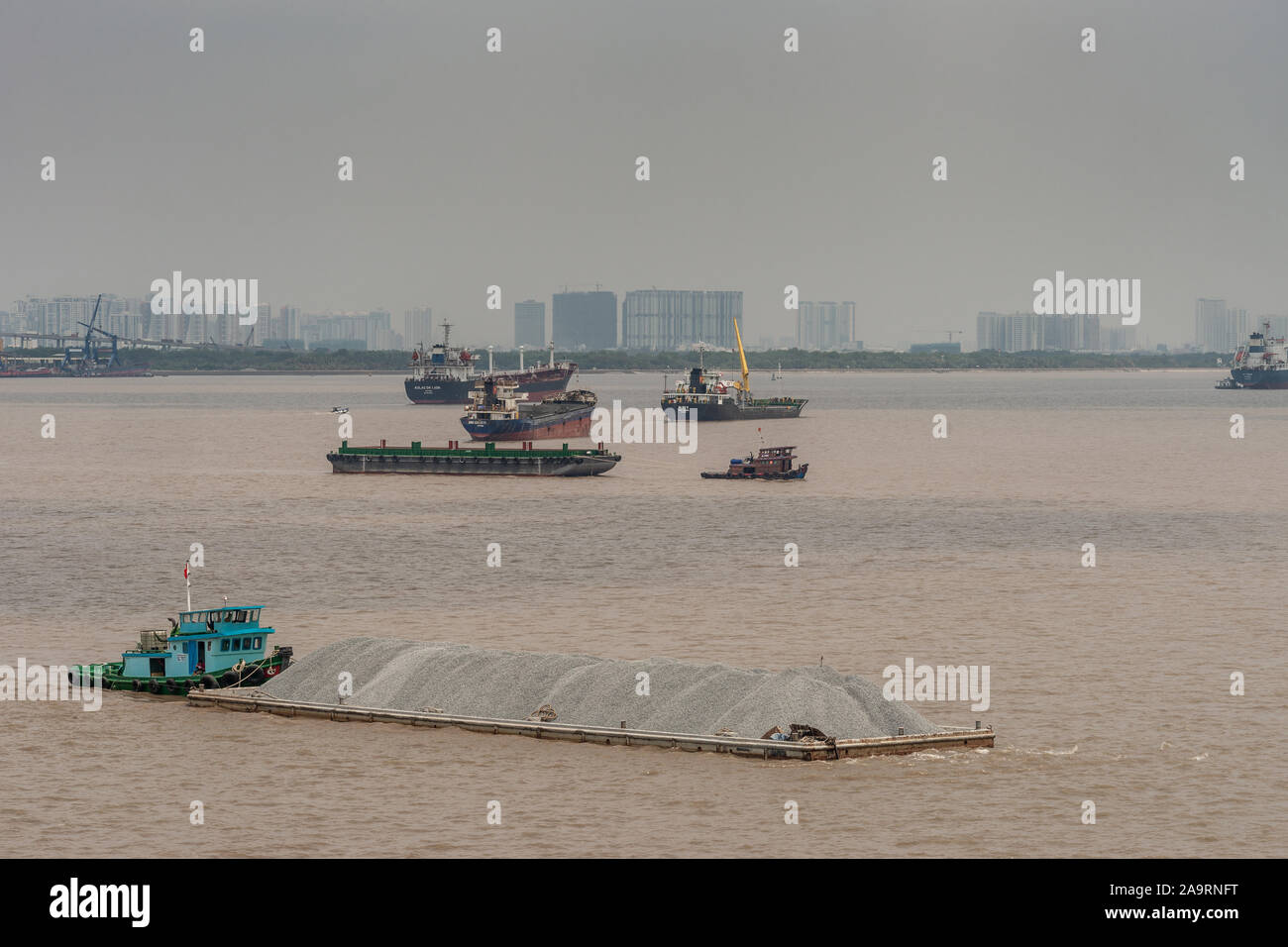Tau Long River, au Vietnam - 12 mars 2019 : Petit bateau bleu pousse longue péniche remplie de pierres gris brun sur le fleuve. D'autres navires et des bâtiments o Banque D'Images