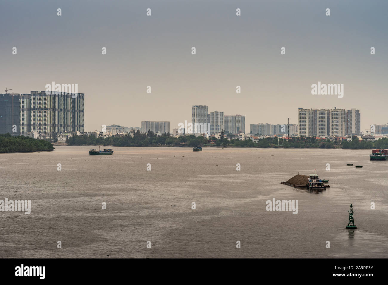 Ho Chi Minh City Vietnam - 12 mars 2019 : Brown chanson fleuve Sai Gon avec quelques petits bateaux. Ceinture verte avec des immeubles de grande hauteur derrière sous la lumière bl Banque D'Images