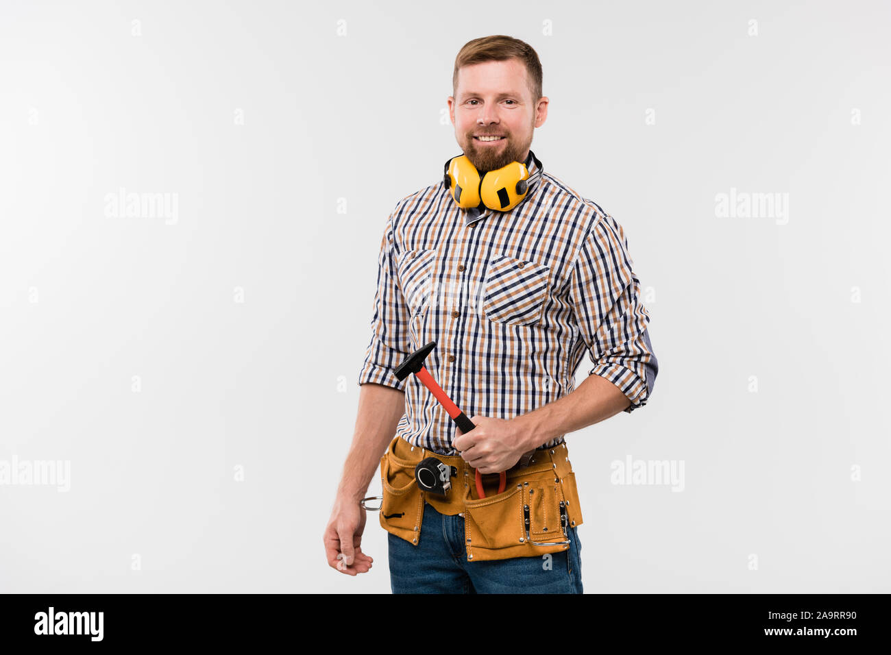 Technicien en souriant barbu de protection avec écouteurs, marteau et ceinture d'outils Banque D'Images
