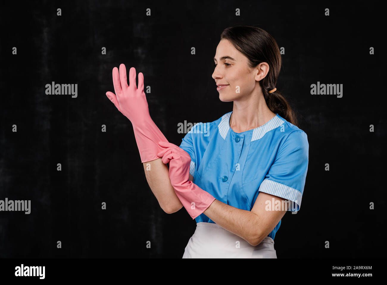 Jeune et Jolie chambre d'hôtel le personnel de service en uniforme bleu de mettre des gants en caoutchouc Banque D'Images