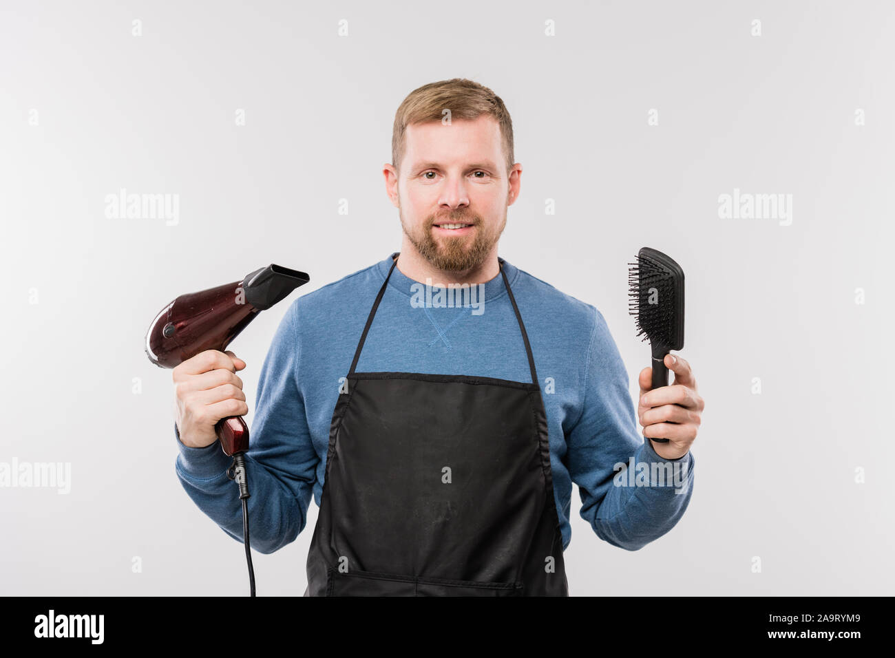 Happy young bearded coiffure en brosse et sèche-cheveux holding tablier Banque D'Images