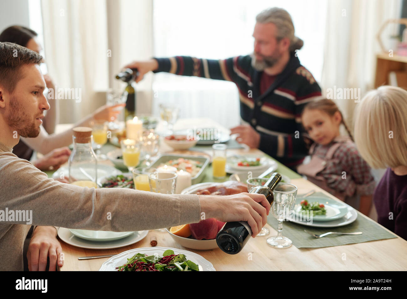 Jeune homme de verser le vin dans le verre de maman assis en face de lui pendant le dîner Banque D'Images