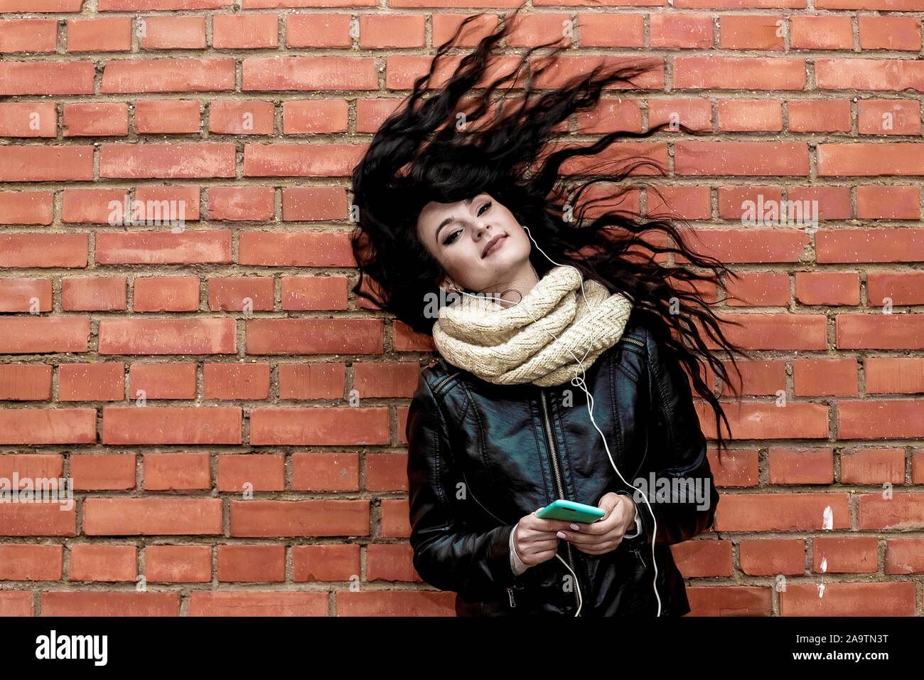 Portrait d'une belle fille brune, sur fond orange dans un vélo et un jean, qui écoute de la musique Banque D'Images