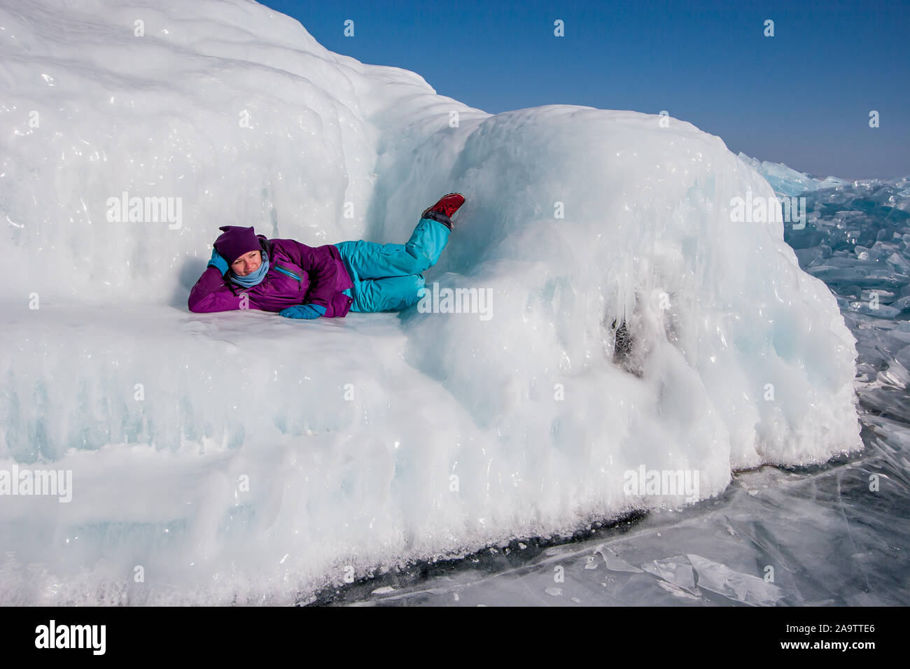 Une jeune fille dans des vêtements d'hiver se trouve sur un immense canapé de glace sur une journée ensoleillée sur le Lac Baïkal. Glace lisse brille au soleil et fondu. Banque D'Images
