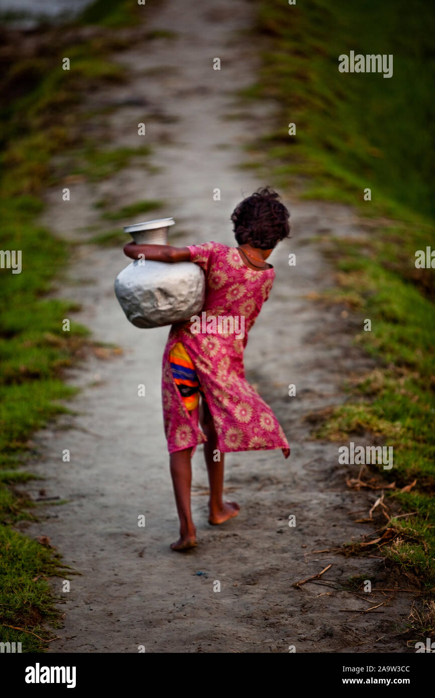 L'eau potable est rare à Nijhum Dweep, l'île du Silence. Une fille transporte de l'eau potable d'un tube loin bien tôt le matin Banque D'Images