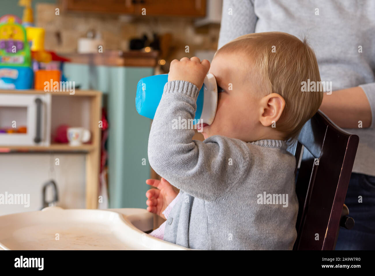 Les jeunes, bébé fille est assise dans sa chaise d'un verre de sa tasse. Banque D'Images