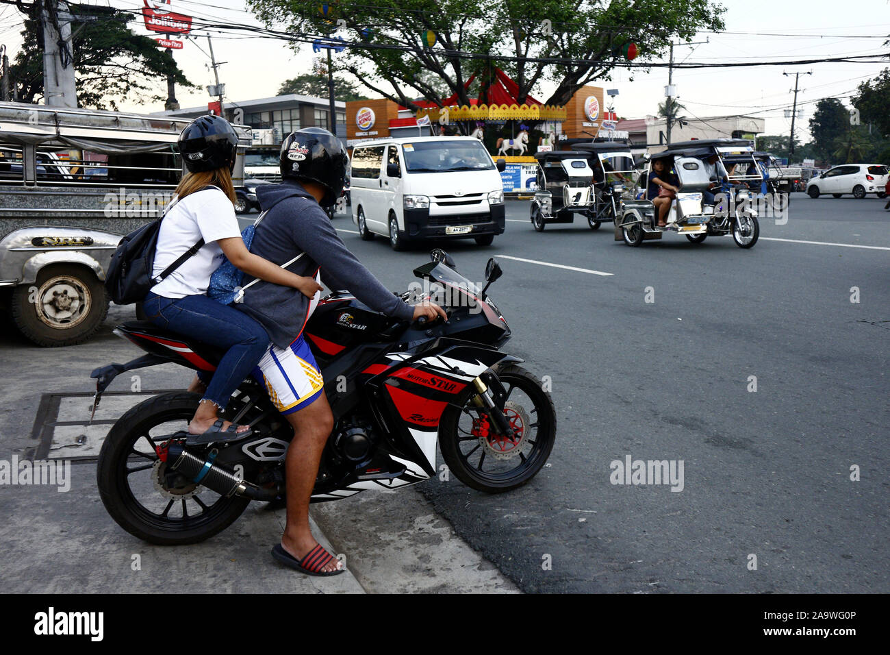 ANTIPOLO CITY, PHILIPPINES - 16 NOVEMBRE 2019 : pilote de moto et son passager se préparer à traverser une route très fréquentée. Banque D'Images