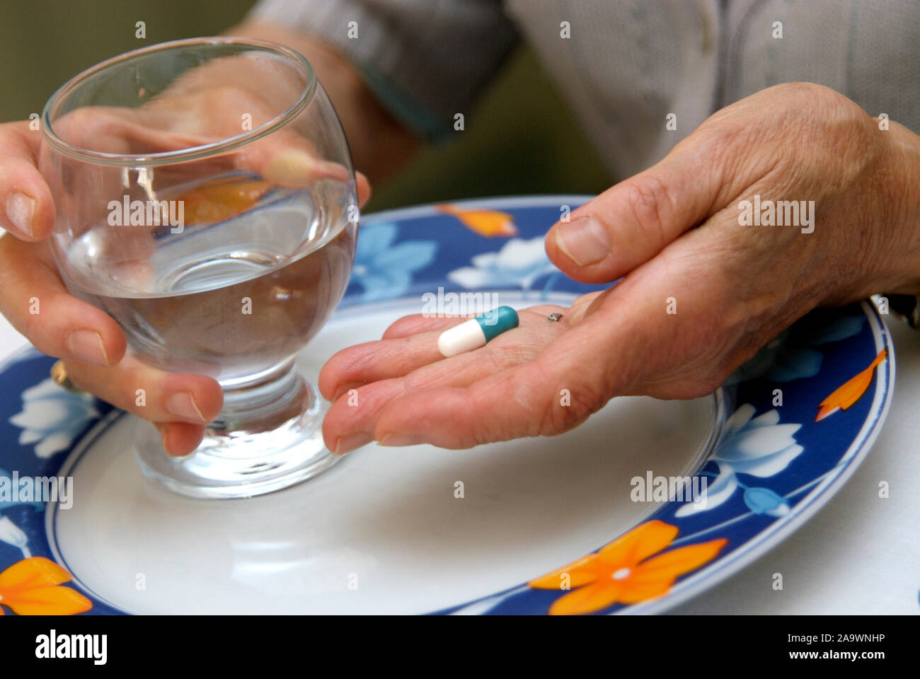 Mains d'une vieille femme tenant un comprimé et un verre d'eau Banque D'Images