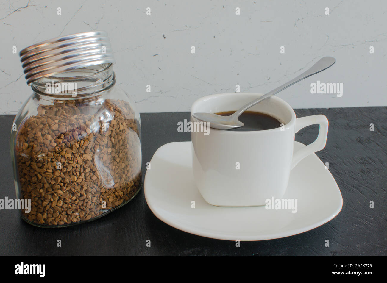 Un bocal de verre de café instantané en granules à côté d'une grande tasse blanche. Banque D'Images