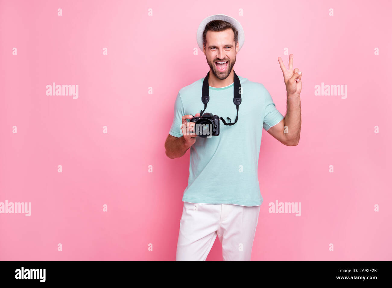 Portrait de l'homme drôle funky amoureux du tourisme ont vacances de printemps tenir dlsr caméras faire v-sign wear tee-shirt bleu pantalon blanc isolated over Banque D'Images