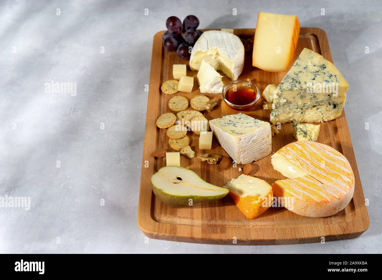 De nombreuses sortes de fromages servi sur planche de bois avec des noix, raisins sur fond clair. Copy space Banque D'Images