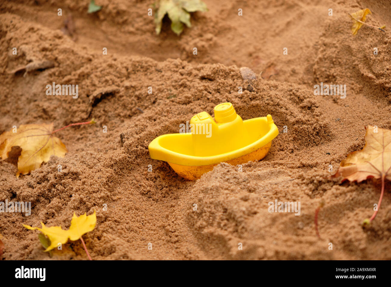 Petit bateau jouet en plastique jaune est dirving à travers le sable avec les feuilles d'automne dans la carrière de sable sur une aire de jeux Banque D'Images