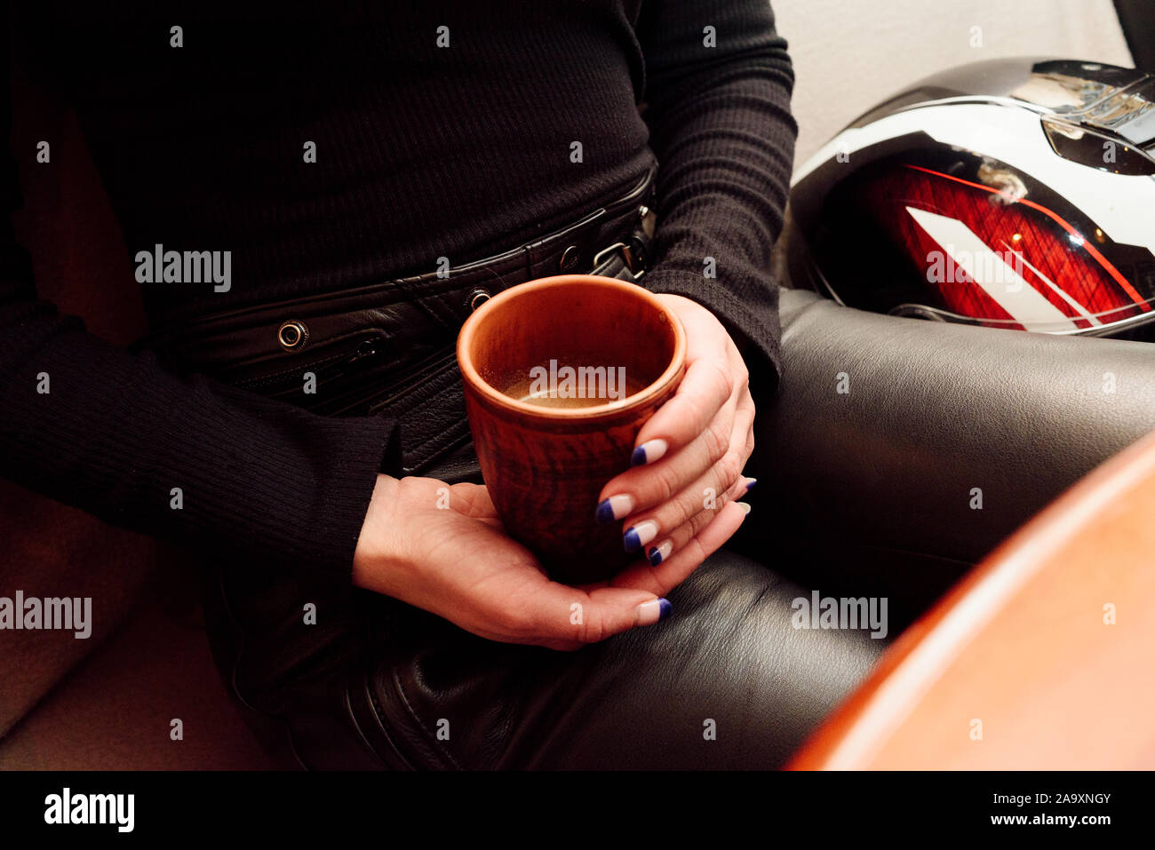 Dans les mains des femmes chandail chaud holding tasse de café. Close up. Une tasse de café dans les mains d'une fille et d'un casque pour une moto. Jeune fille en noir cuir Banque D'Images