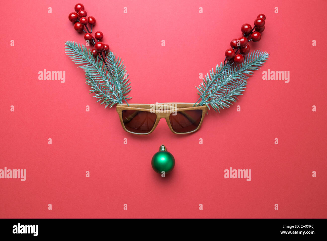 Le renne face en décorations de Noël, des lunettes, des baies de houx et des branches de pins. Concept minimal. Mise à plat Banque D'Images