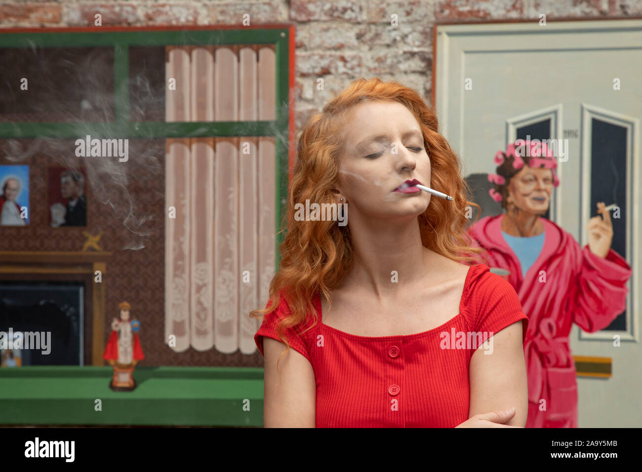 Jeune femme readheaded cigarette contre Wall Graffiti, Tribunal de Commerce, Belfast, en Irlande du Nord Banque D'Images