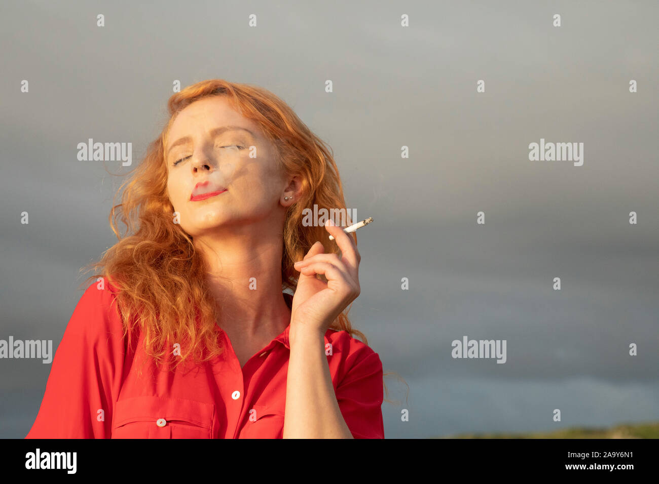 Rousse femme irlandaise fumeurs cigarette sur la plage de Sunny Irlande du Nord Banque D'Images