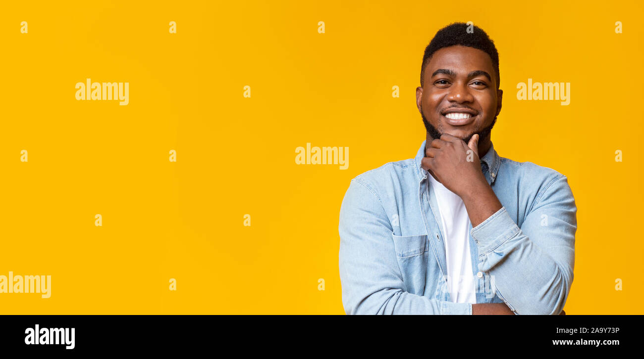 Smiling african guy de toucher sa barbe sur fond jaune Banque D'Images
