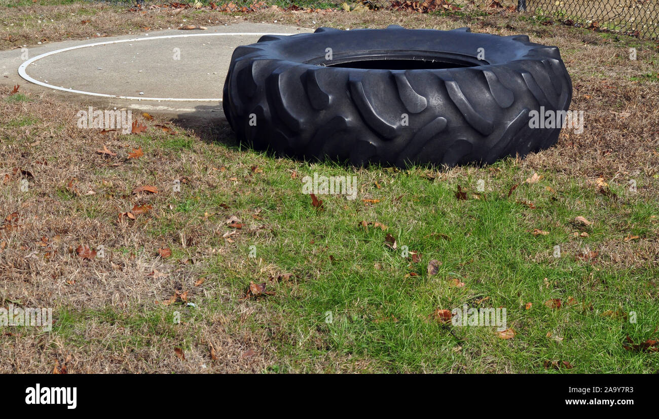 Un grand noir le pneu du tracteur utilisé pour l'entraînement par les athlètes. C'est dans l'herbe et il y a une cible cercle derrière le pneu. Il y a de la place pour le texte. Banque D'Images
