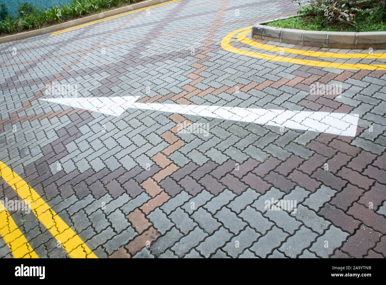 Flèche blanche et doubles lignes jaunes peintes sur interlocking concrete pavement Banque D'Images