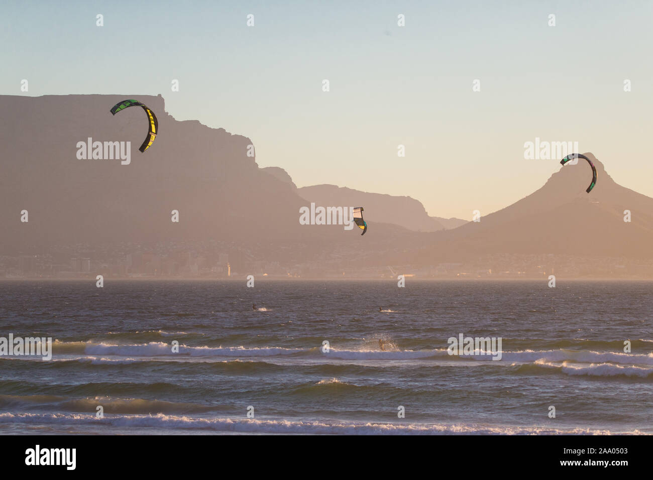 Kite surfeurs en action, les vagues au coucher du soleil à Bloubergstrand, Cape Town, Afrique du Sud avec la Montagne de la Table et Lions Head dans l'arrière-plan Banque D'Images