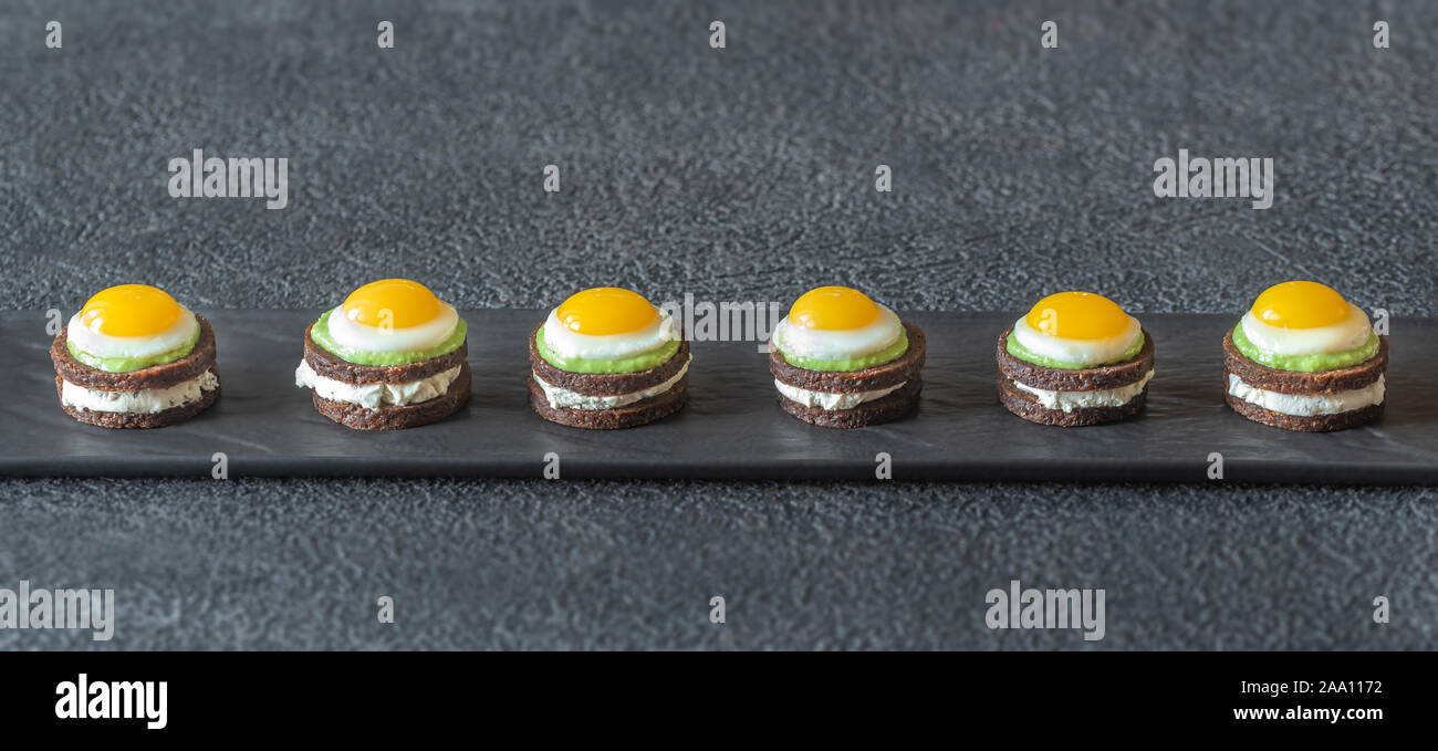 Canape avec fromage à la crème, guacamole et oeufs de caille frit sur la plaque Banque D'Images