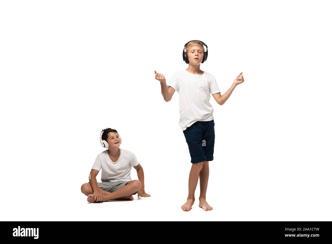 Joyeux garçon assis les jambes croisées et à la danse au frère de casque sur fond blanc Banque D'Images