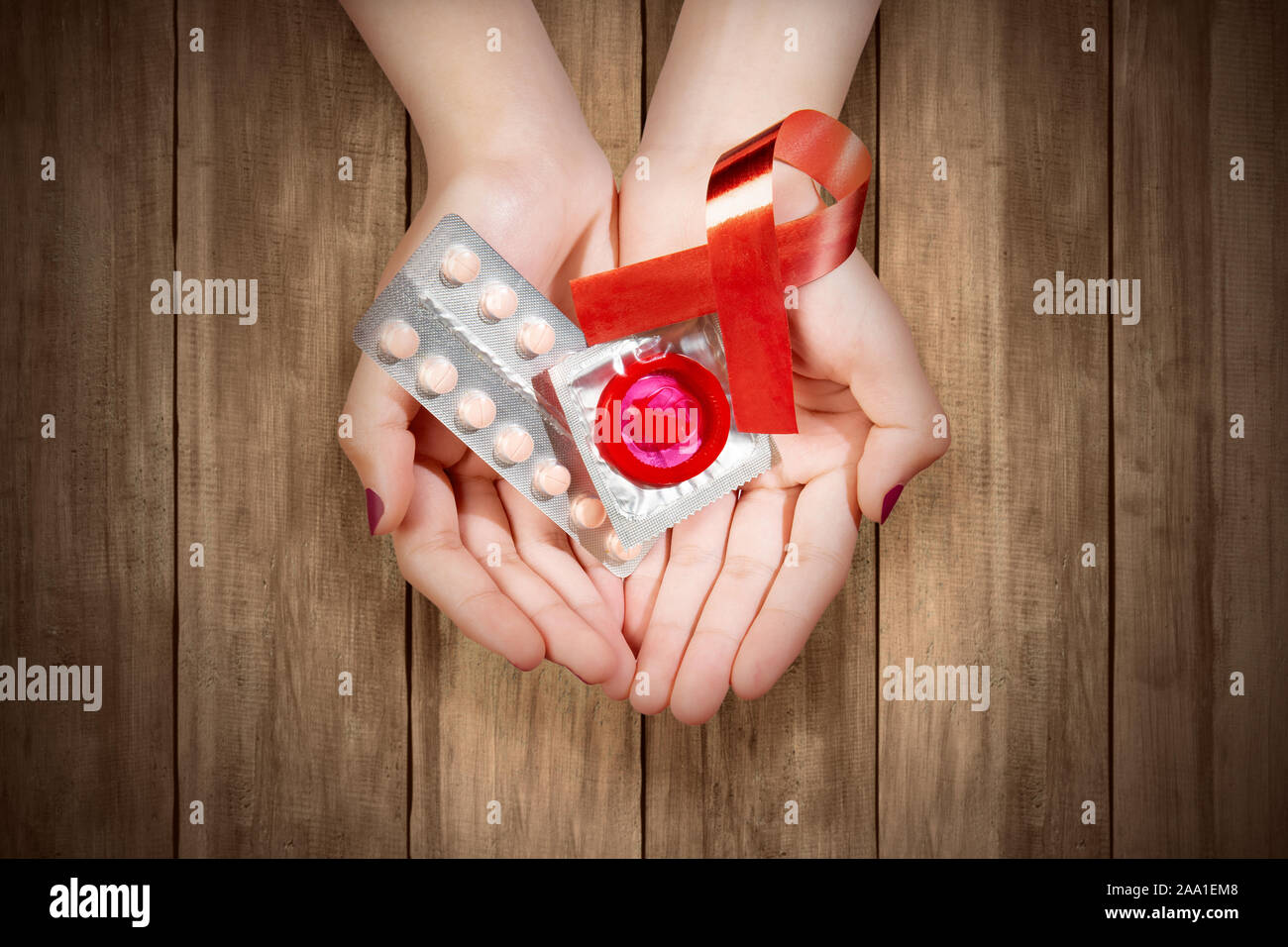 Des mains humaines montrant ruban rouge, pilules contraceptives, et d'un condom. Le Vih Sida sensibilisation ruban Banque D'Images