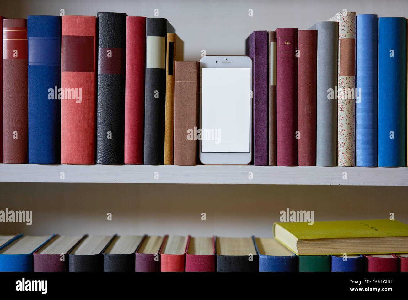 Téléphone mobile entre livres colorés dans une étagère Banque D'Images