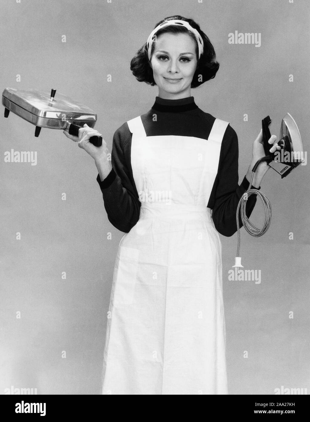 Dans les années 60. Une jeune femme tient un fer à repasser et un fer à repasser électrique fait whaffle par Elektro Helios. Suède 1963 Banque D'Images
