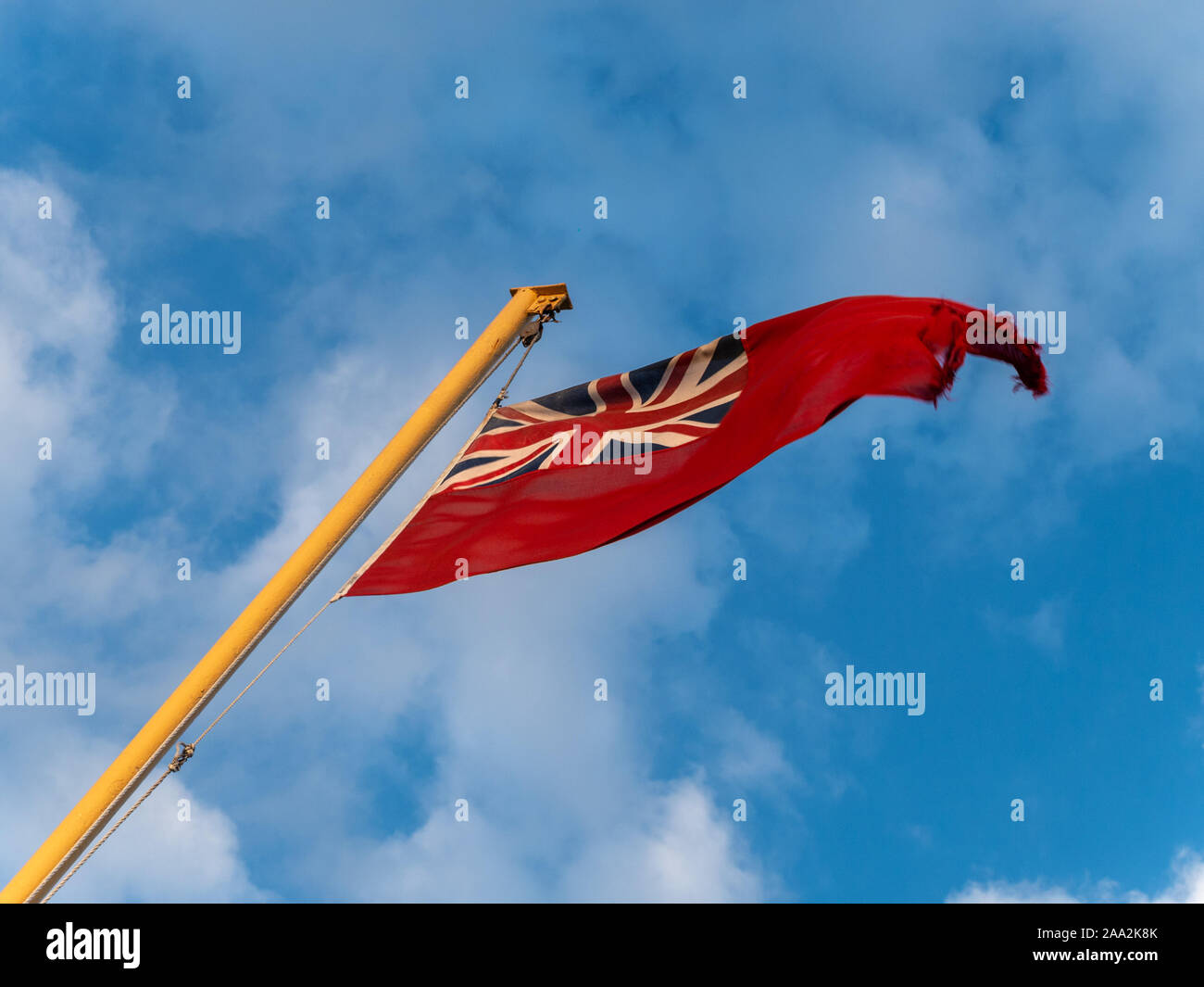 Red Ensign britannique effiloché de vol flagstaff contre le ciel bleu. Banque D'Images