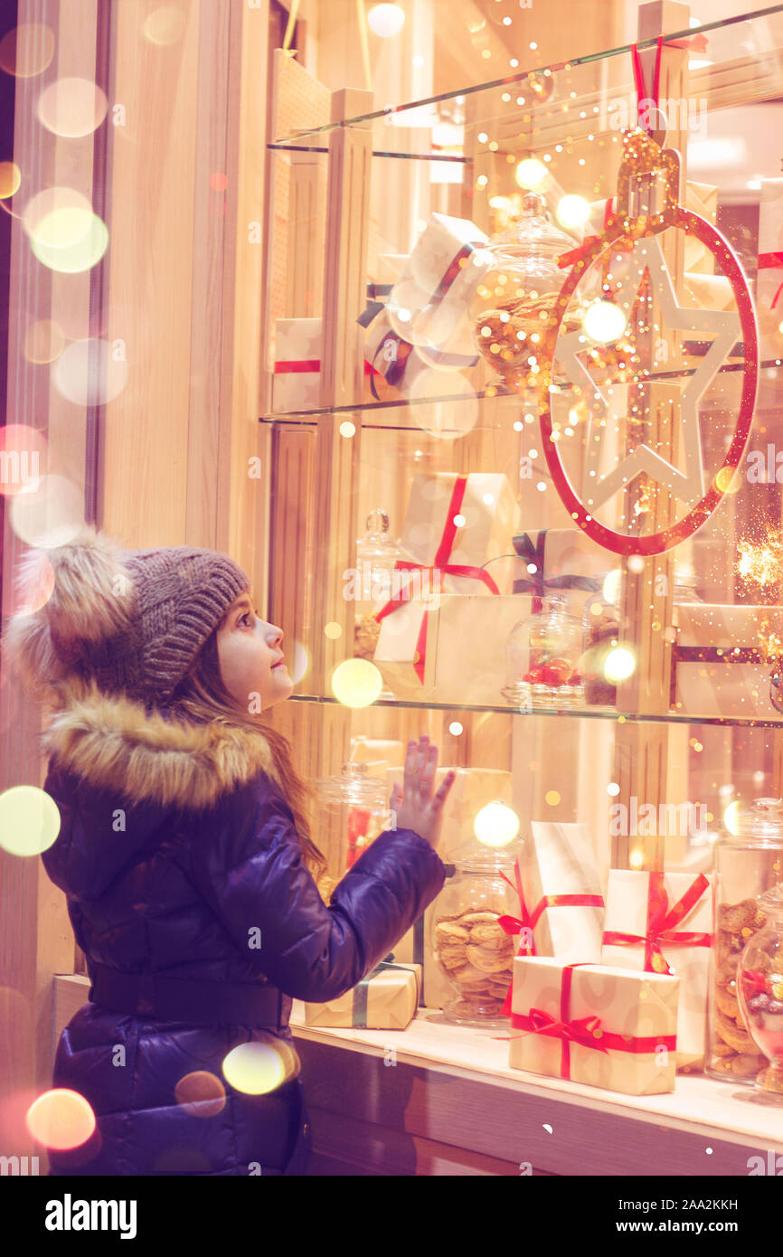 Belle petite fille en face de confiserie, décorées avec des cadeaux emballés et des bonbons. Concept de Noël, window shopping Banque D'Images