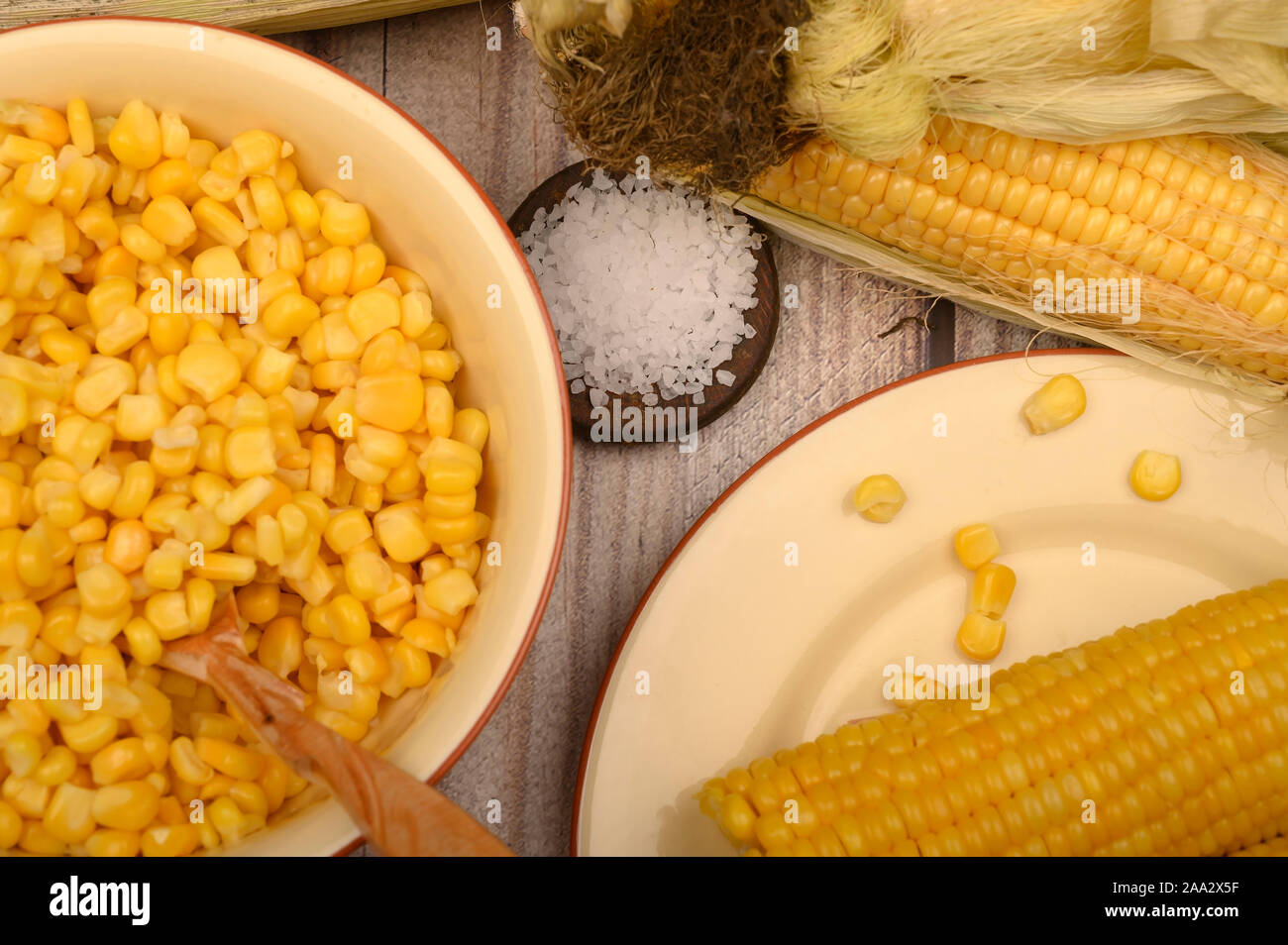 Grains de maïs doux dans une assiette avec une cuillère en bois, le gros sel et les épis de maïs sur la table. Régime alimentaire sain. Régime alimentaire de remise en forme. Pour une petite douceur. Fermer u Banque D'Images