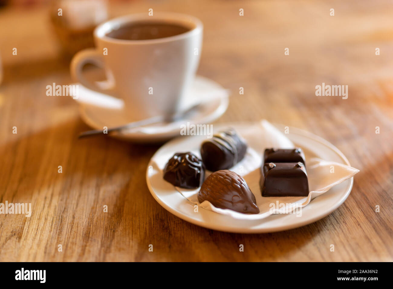 Une tasse de chocolat chaud et des chocolats artisanaux de différentes formes, sur une table en bois dans un café avec lumière tamisée et une ambiance chaleureuse Banque D'Images