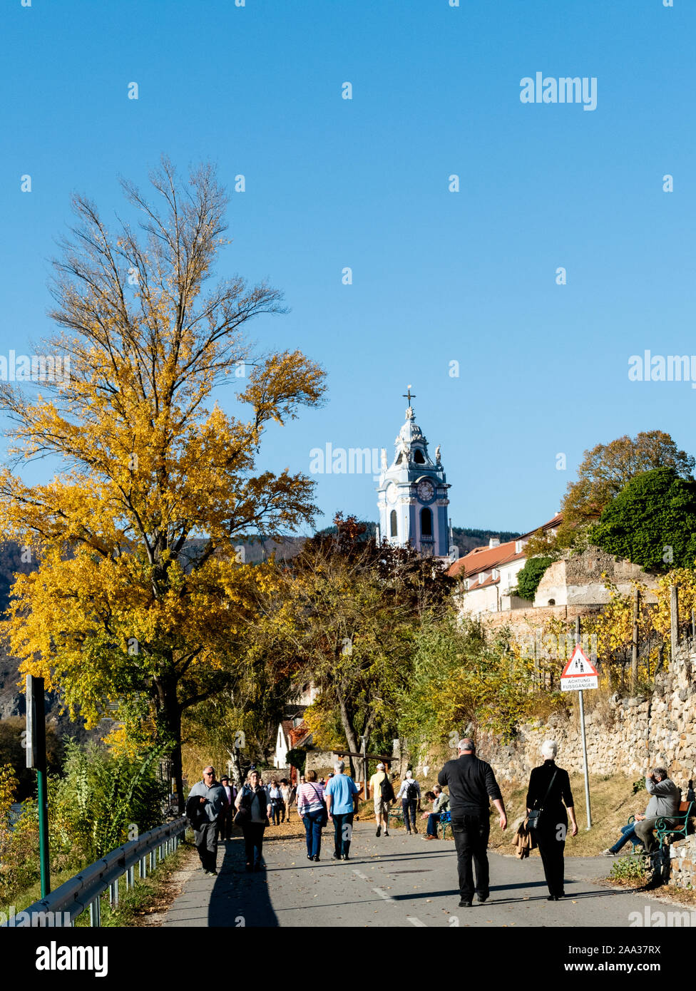 Les touristes à marcher le long de la Danube banque à Durnstein, l'Autriche, avec le monastère en arrière-plan Banque D'Images