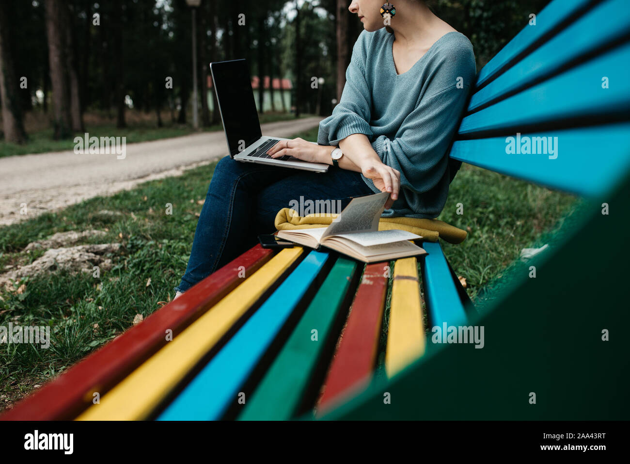 Fashionable young Caucasian woman sitting on bench in park en bois coloré. Elle est saisie sur ordinateur portable. Travail freelance concept. L'espace de copie pour le texte Banque D'Images