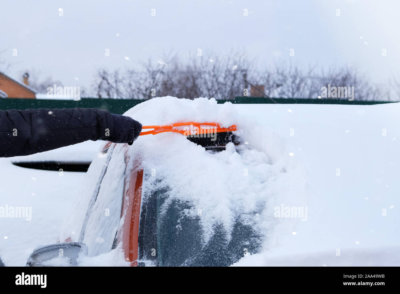 Pinceau en main. mans L'homme s'efface pare-brise de voiture orange à partir de la neige. Voiture couverte de neige. Problèmes d'hiver des automobilistes. Enneigé. Banque D'Images