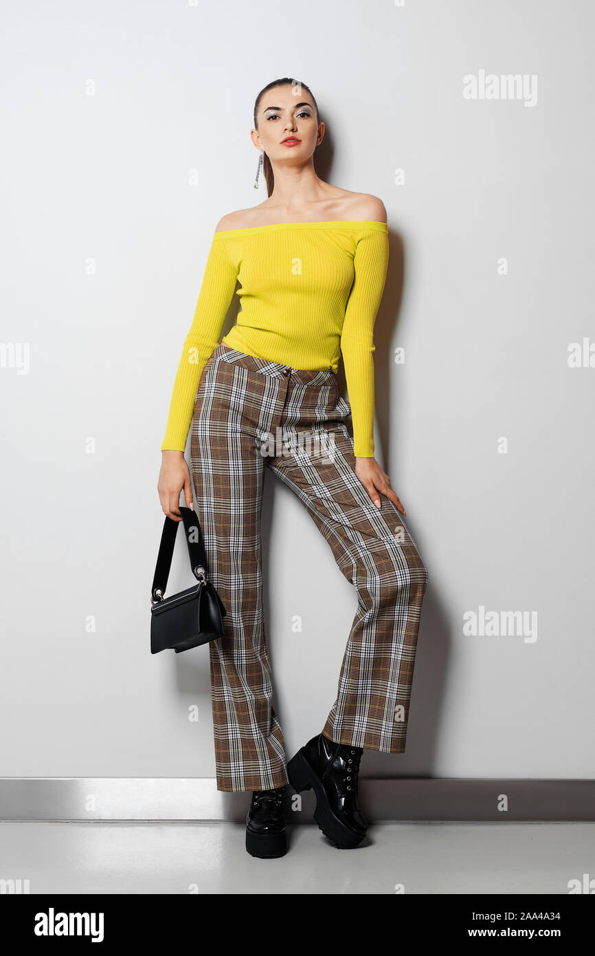 Fille en pantalon et pull jaune à carreaux avec petit sac à main posant  près de mur blanc Photo Stock - Alamy