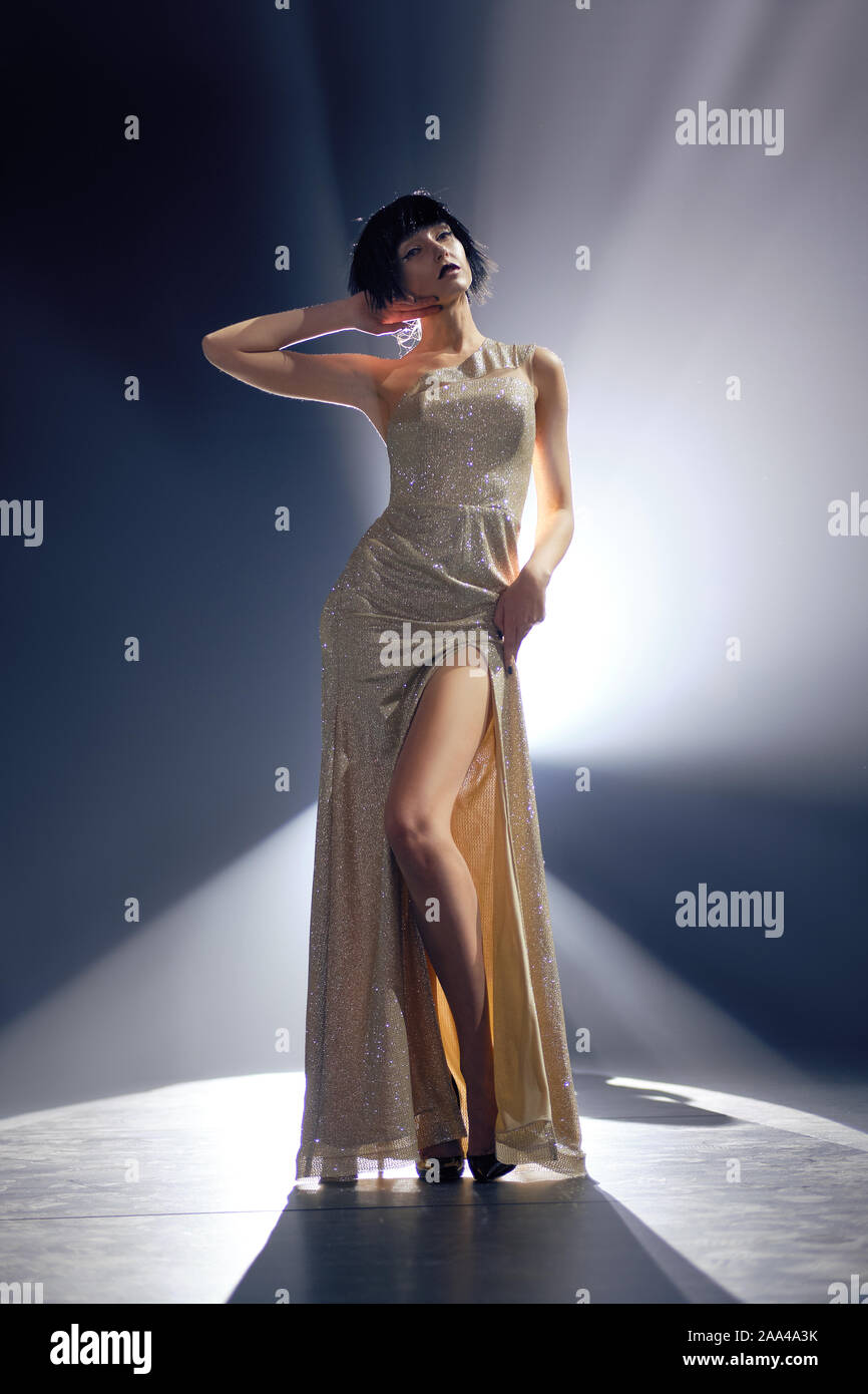 Fashion model en robe longue avec une profonde coupure sur la scène sous la lumière clé Banque D'Images