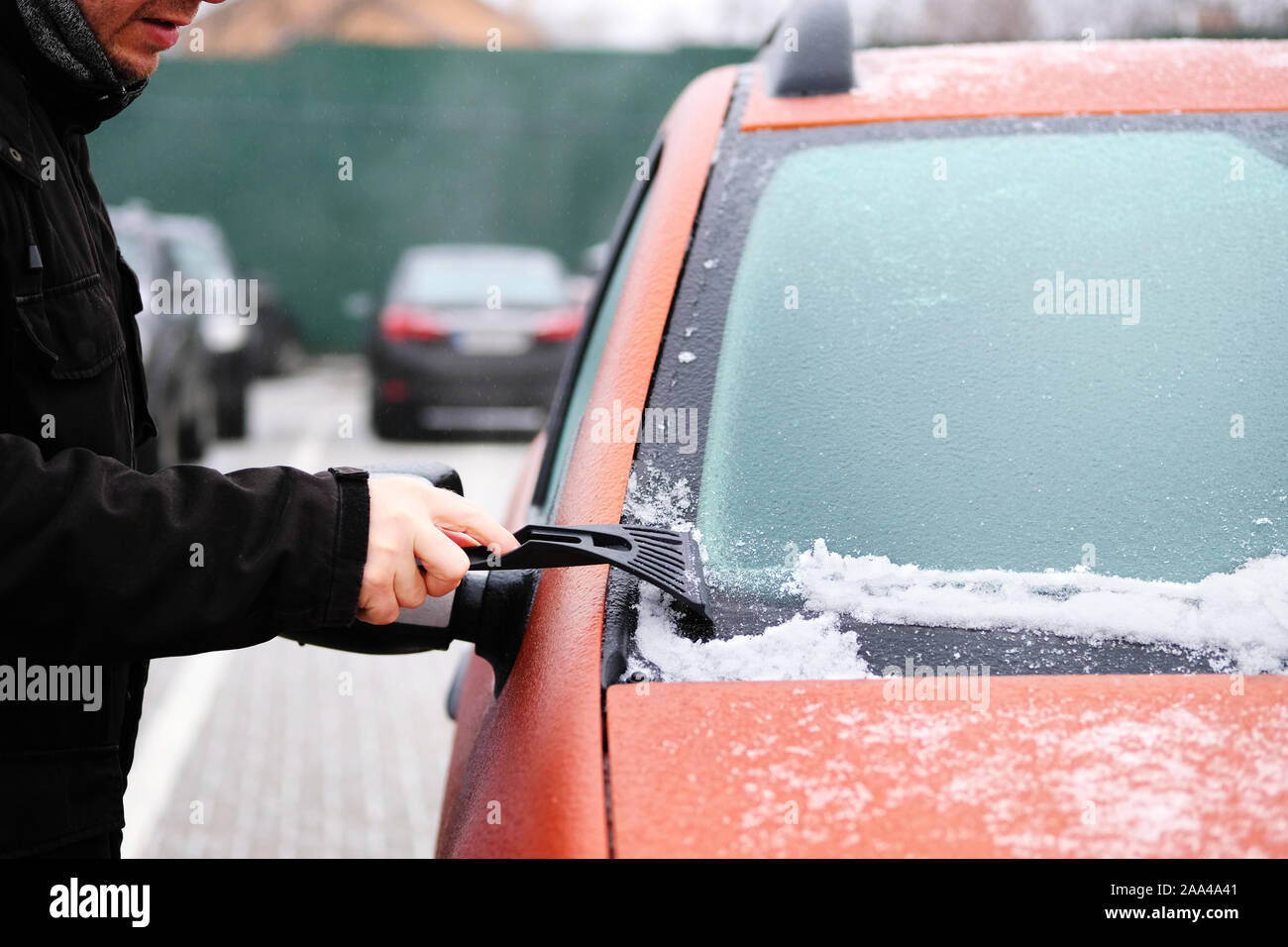 Efface l'homme de neige-glace glace de voiture. Le racloir en mans main. Fenêtre d'orange congelé de nettoyage automobile. Banque D'Images
