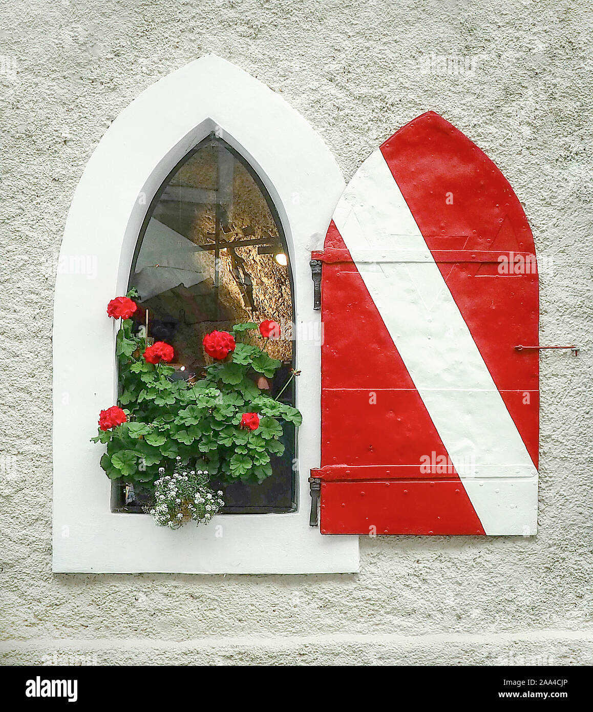 Plante géranium rouge dans un style européen arch fenêtre avec rayures rouges et blanches et de porte arrière allumé crucifix Banque D'Images