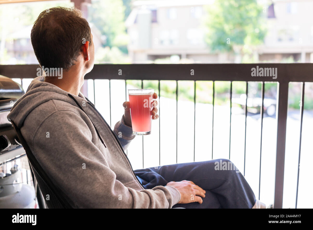 Homme assis à l'extérieur en fauteuil drinking glass of red pink lemonade jus cocktail sur condo appartement balcon à Colorado mountain town looking at view o Banque D'Images