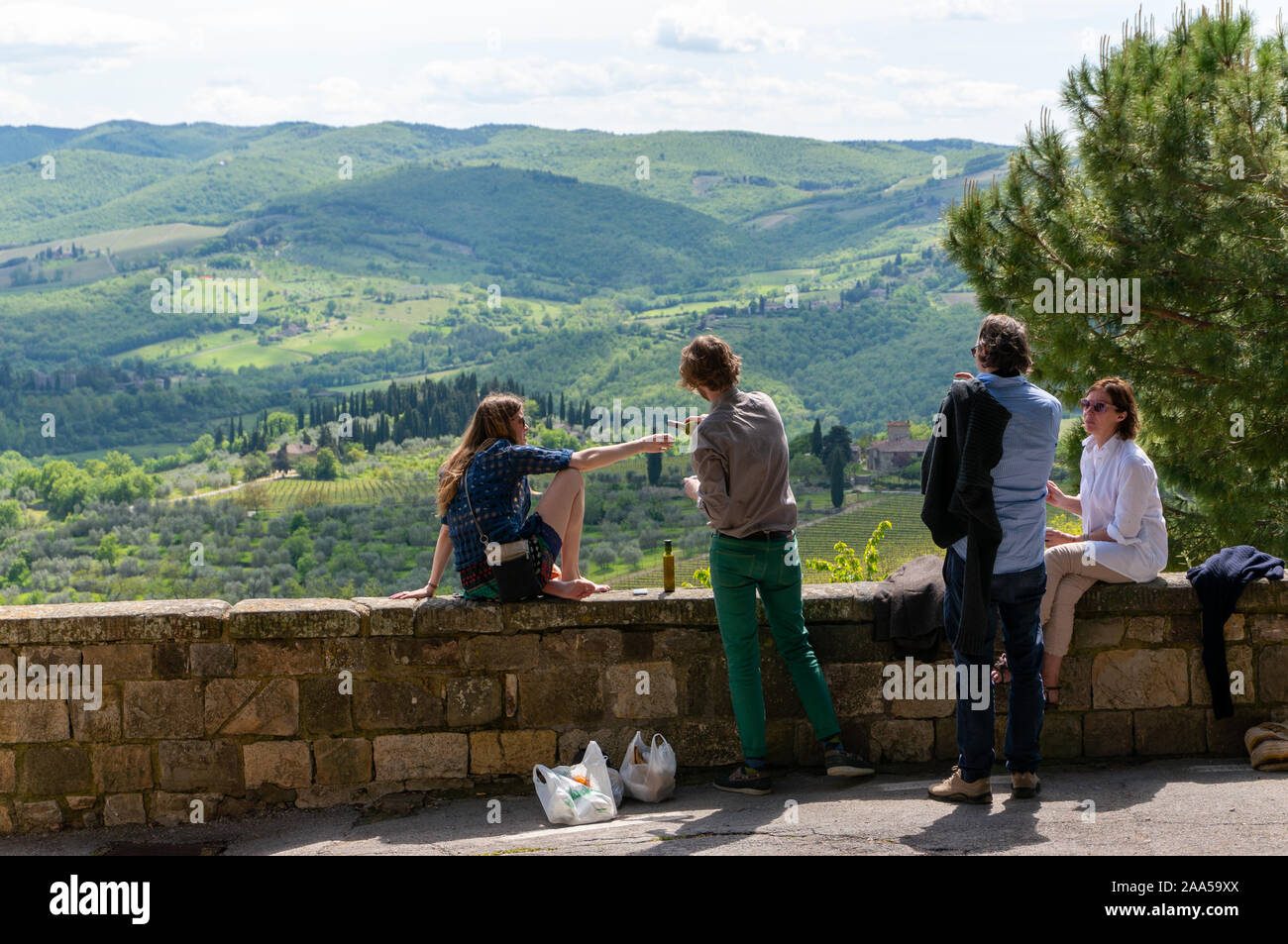 Les jeunes gens assis sur un mur en pierre surplombant la vallée fertile profitant de vin et le pain ensemble, Toscane, Italie Banque D'Images