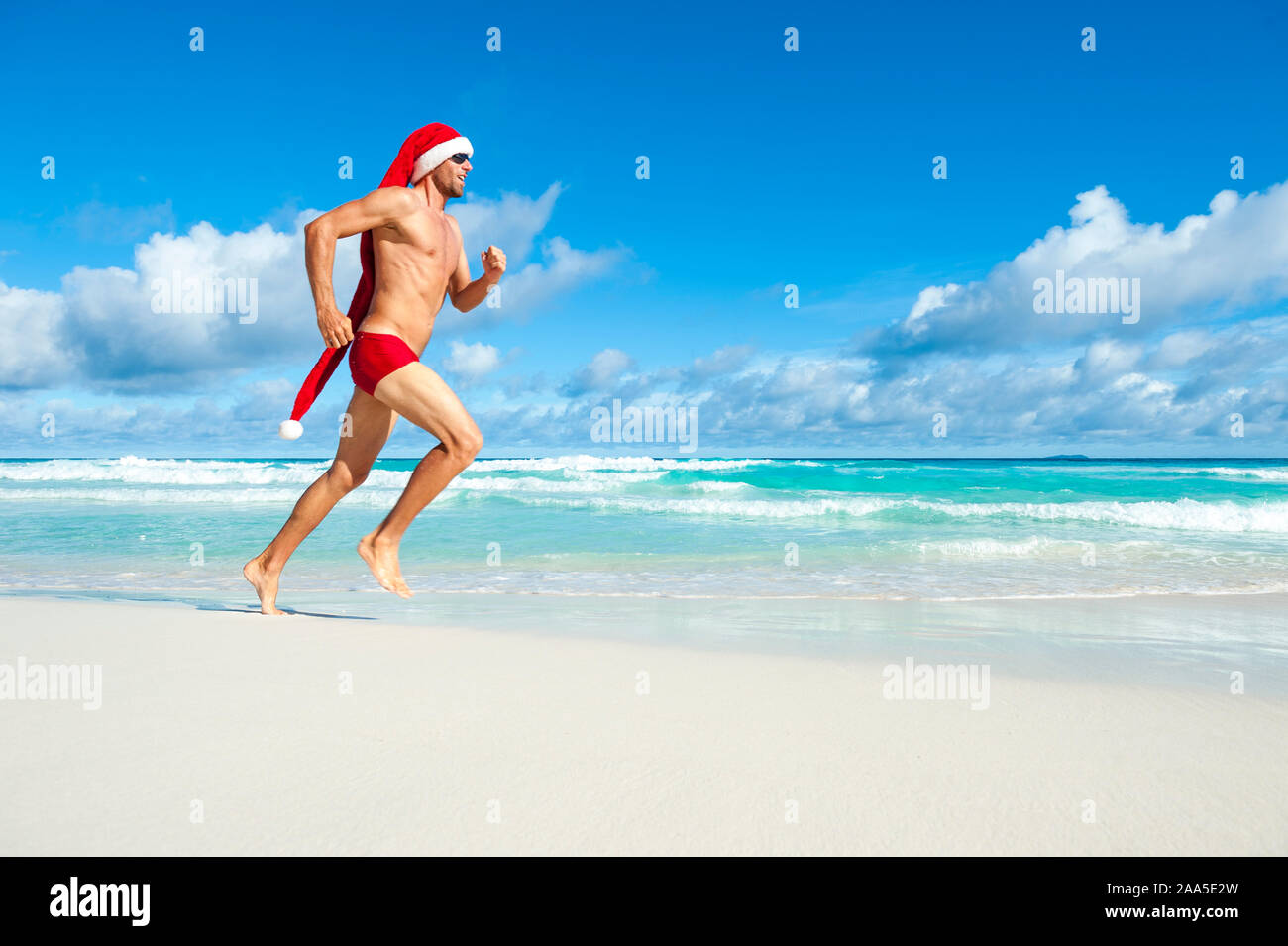 Santa athlétique avec de longues hat exécutant en rouge sport mémoires sur le rivage d'une plage tropicale dans une routine d'entraînement de Noël Banque D'Images