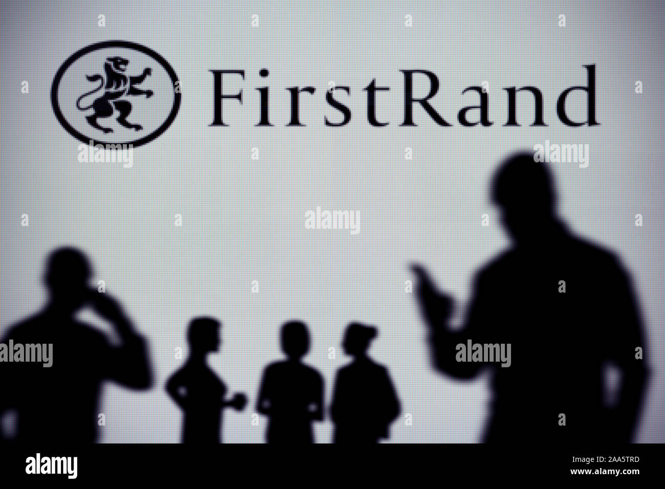 La FirstRand Bank logo est visible sur un écran LED à l'arrière-plan tandis qu'une silhouette personne utilise un smartphone (usage éditorial uniquement) Banque D'Images