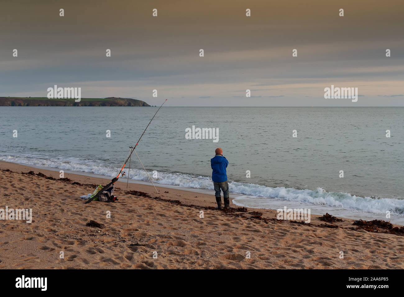 Un pêcheur solitaire est à la recherche à la mer durant le coucher du soleil à St Austell, Cornwall, Royaume-Uni. Banque D'Images