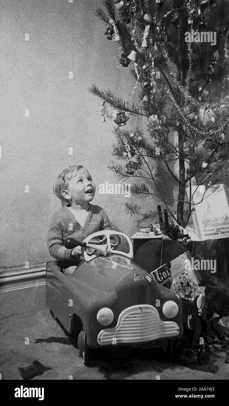 Années 1960, historique, par un arbre de Noël, un bébé garçon heureux assis dans le siège de son cadeau de Noël, une nouvelle voiture à quatre roues de jouet. Banque D'Images