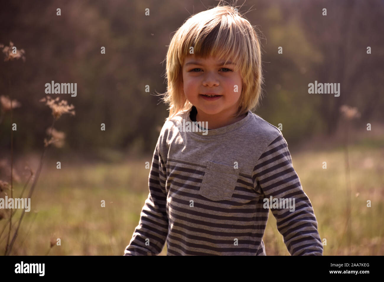 Portrait en gros plan d'un petit garçon aux cheveux blonds et marcher sur un champ de printemps smiling at the camera Banque D'Images