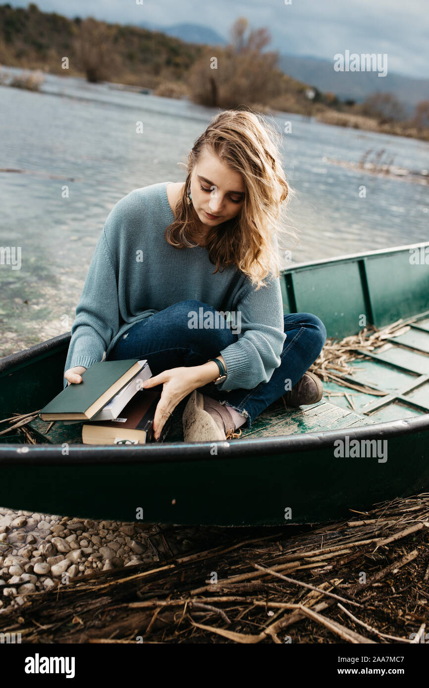 Portrait de la jeune belle femme assise sur un bateau et lecture d'un livre. Elle est bookworm et elle choisit entre quelques livres. Banque D'Images